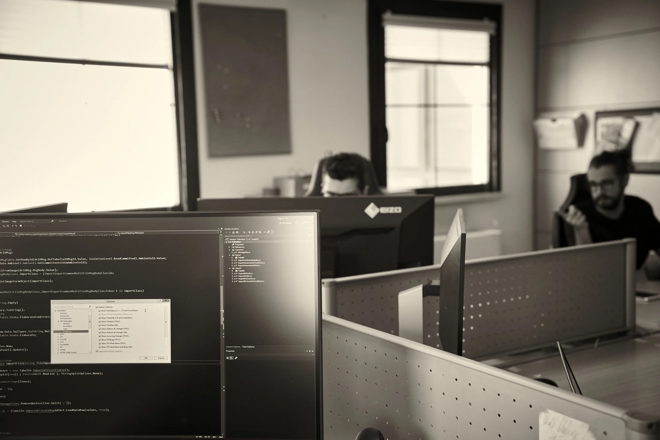 Developer che analizza codice e dati su una postazione a doppio monitor in un ufficio open space