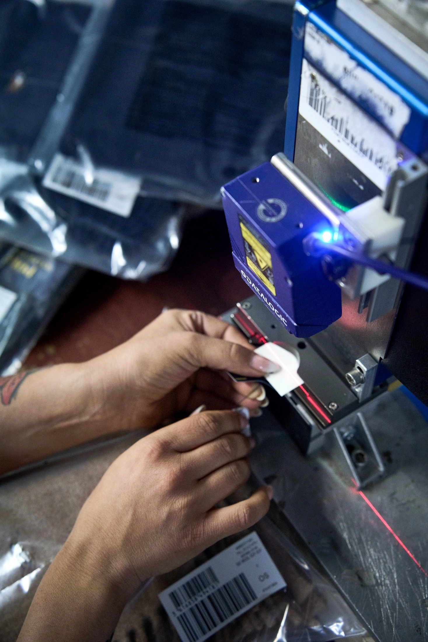 Delle mani posizionano il tag di un capo sotto uno scanner industriale, con luce blu e fascio laser rosso, a colori
