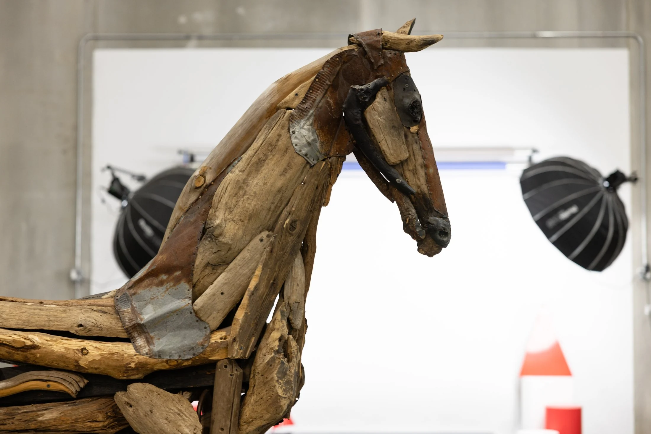 Scultura di cavallo in legno di recupero nel set fotografico interno di un hub logistico non-merchandise Snatt, softbox sullo sfondo, a colori