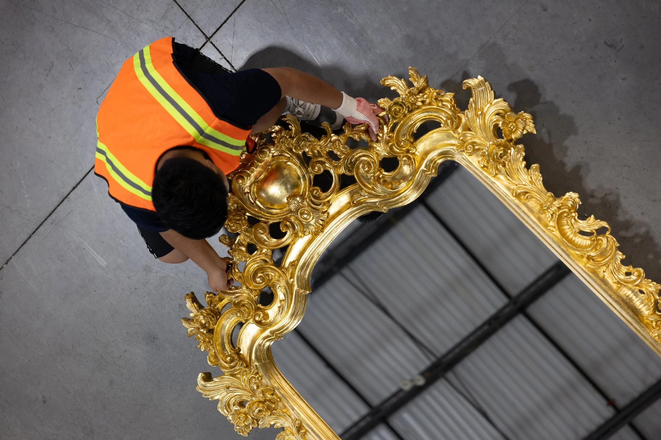 Operatore in gilet alta visibilità che ispeziona dall’alto una cornice dorata ornata, a colori