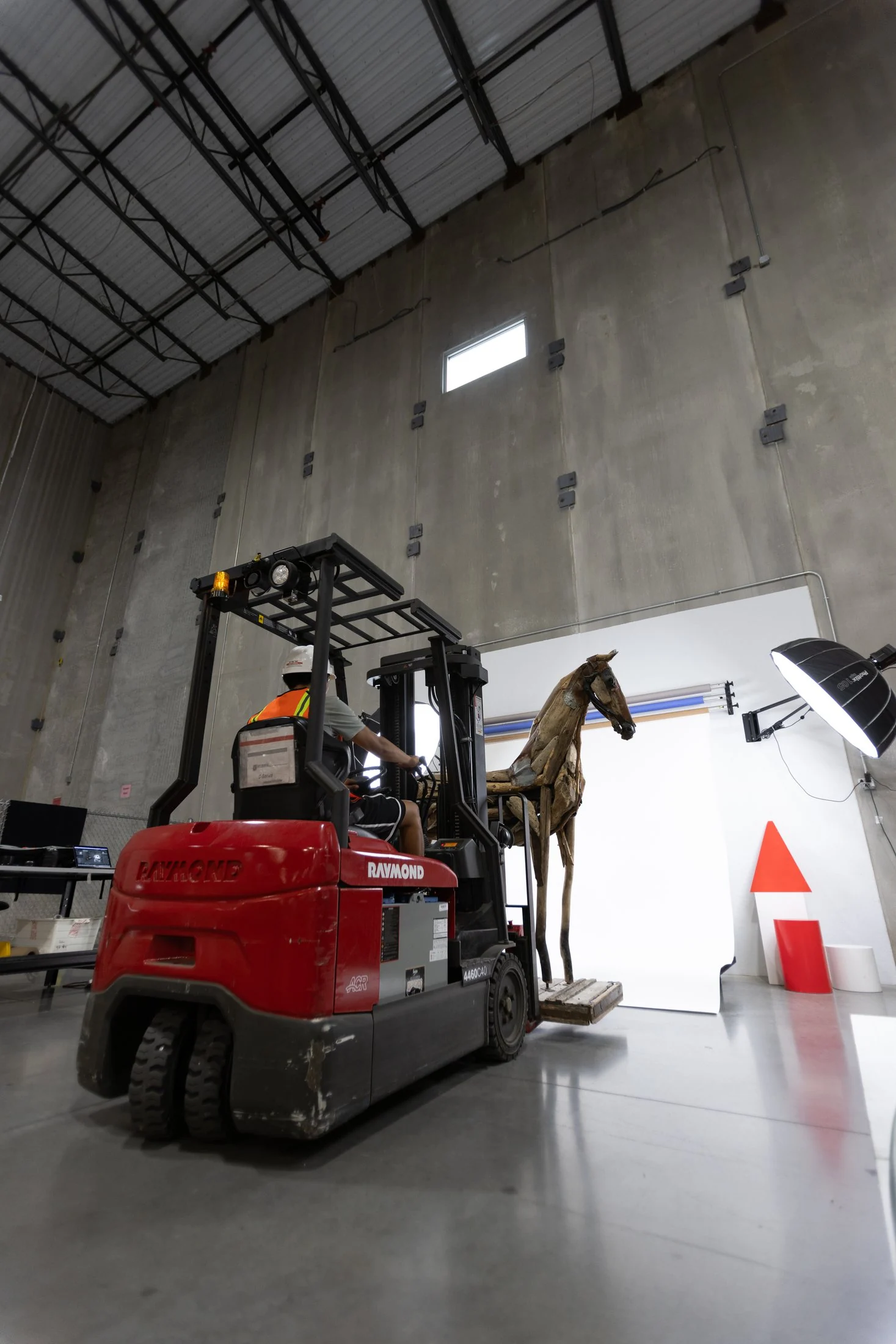 Carrello elevatore che trasporta una grande scultura scenografica attraverso un magazzino alto verso il set fotografico, a colori