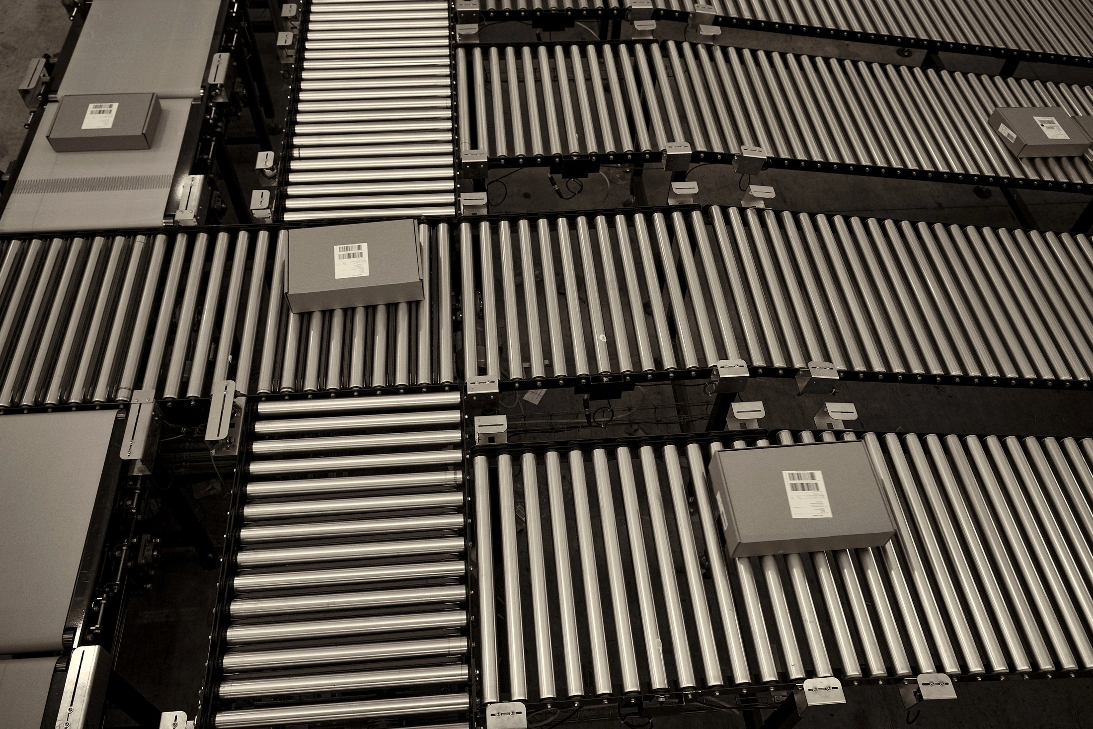 Overhead black and white view of roller conveyors carrying parcels with barcode labels through a Snatt distribution centre