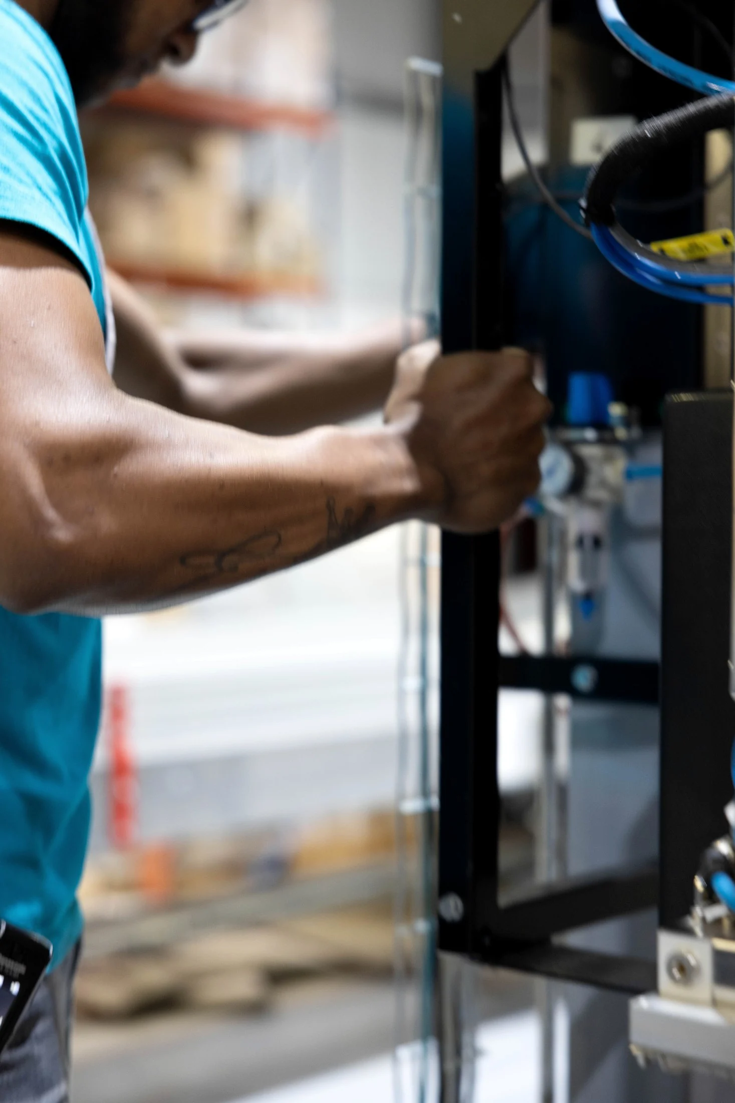 Close up of an operatorโs arm gripping a warehouse racking upright next to automation wiring, in colour