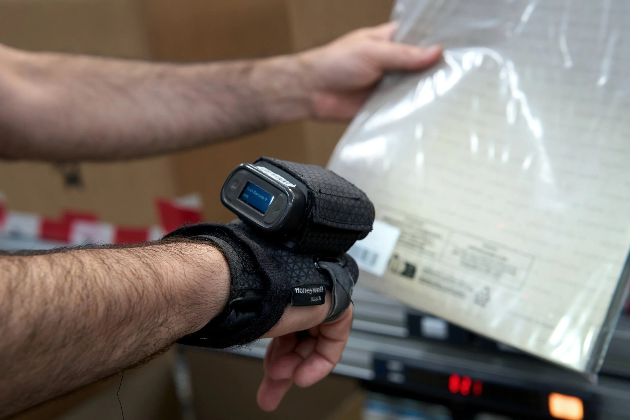 Operator wearing a wrist mounted barcode scanner handles a poly bagged garment on the warehouse floor