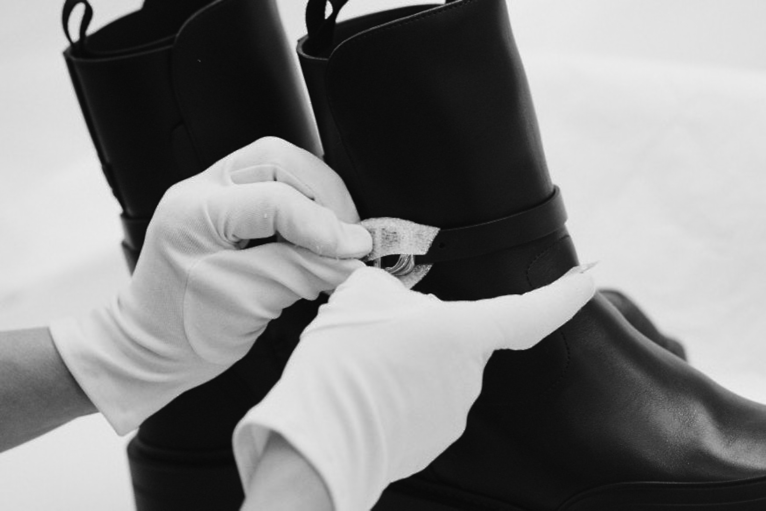 White-gloved hands checking a care label on a leather boot, black and white