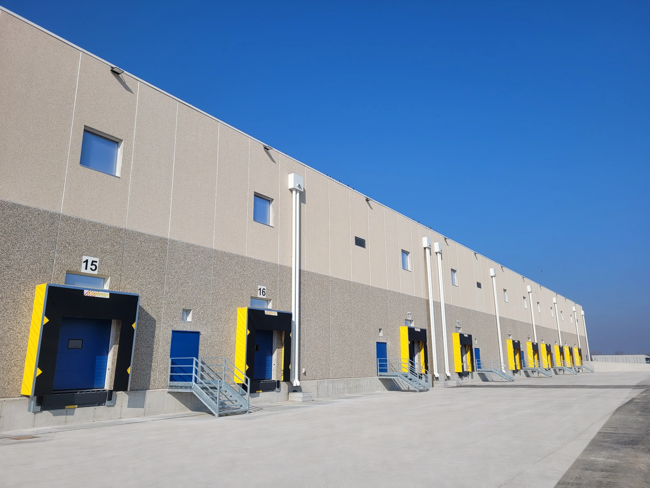 Warehouse facade with numbered loading bays under a clear blue sky, blue and yellow doors