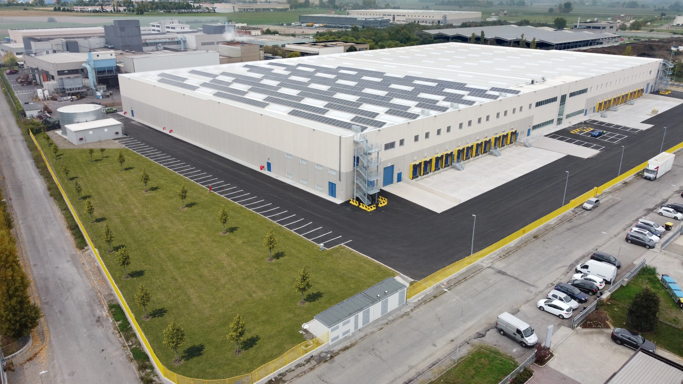 Aerial drone view of a warehouse with a row of yellow loading bays, yard and parking area