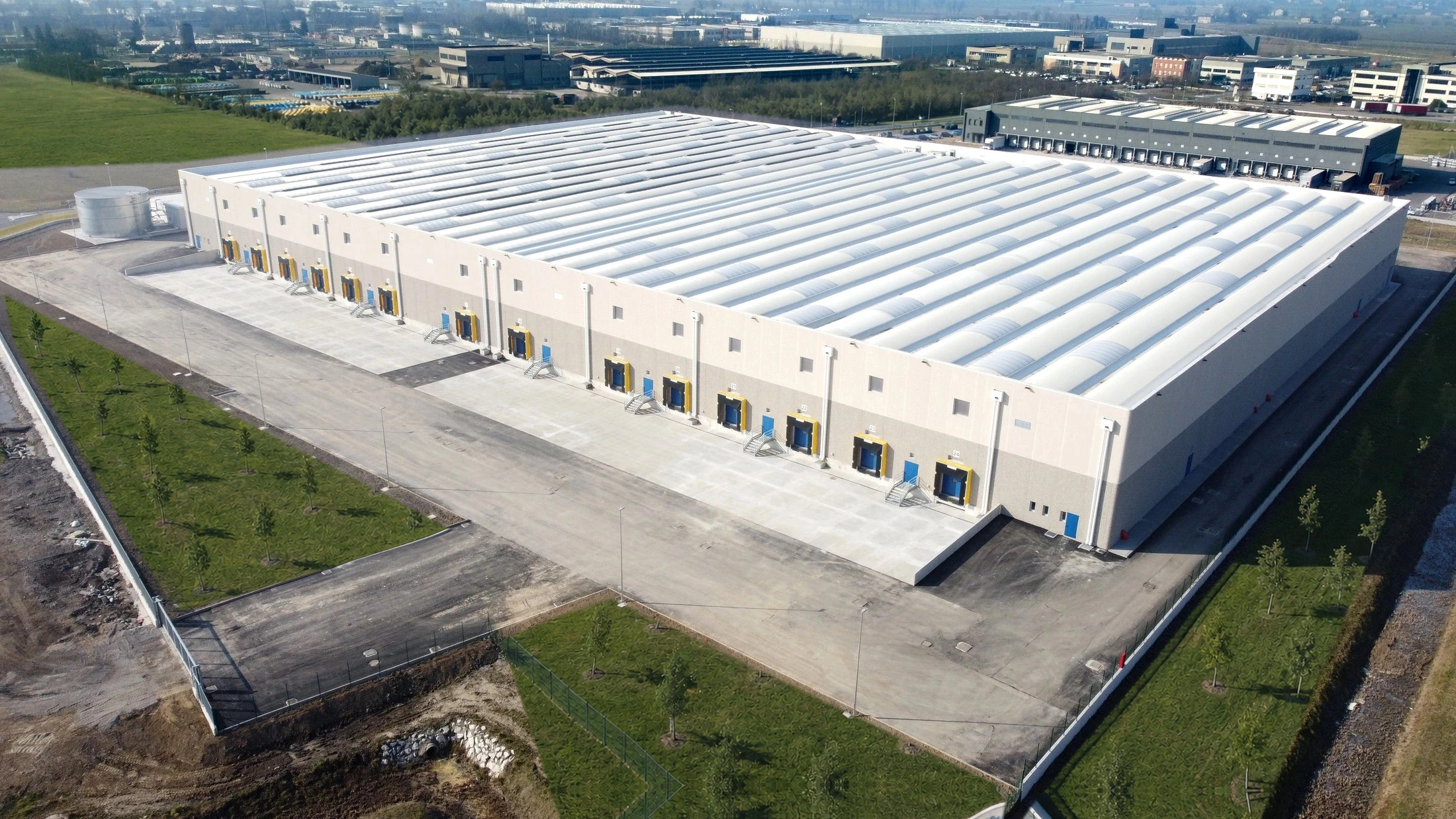 Aerial view of warehouse facade with numbered loading bays and empty concrete yard in morning haze