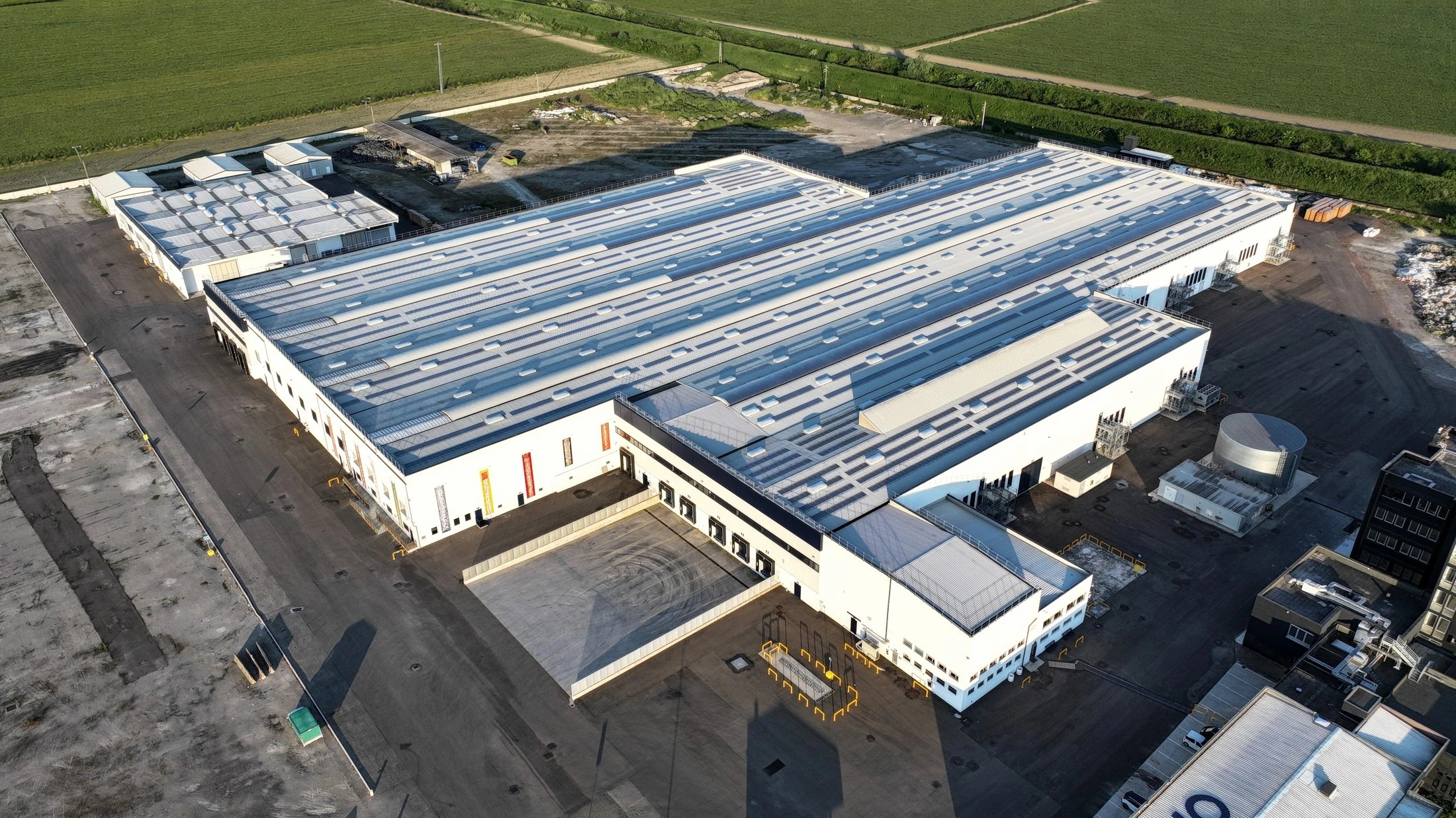 Aerial view of an all-white warehouse building surrounded by open fields, no signage visible